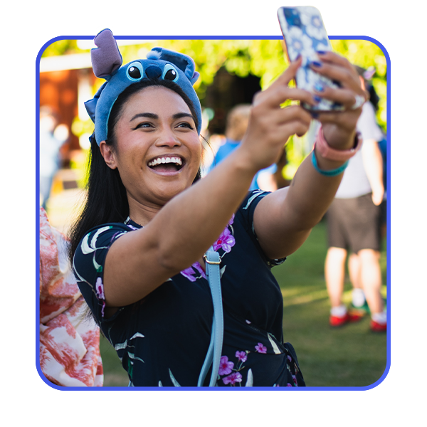 A woman in a dress and a Stitch headband takes a selfie with her cellphone.
