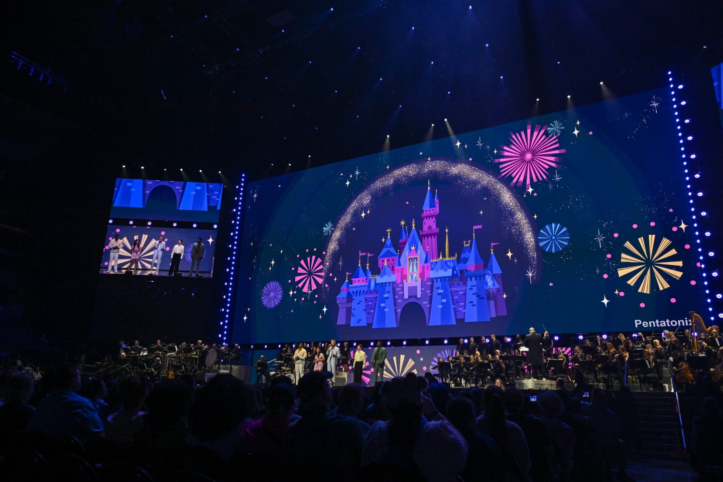 The band Penatonix, standing on large brightly-lit stage at D23: The Ultimate Disney Fan Event