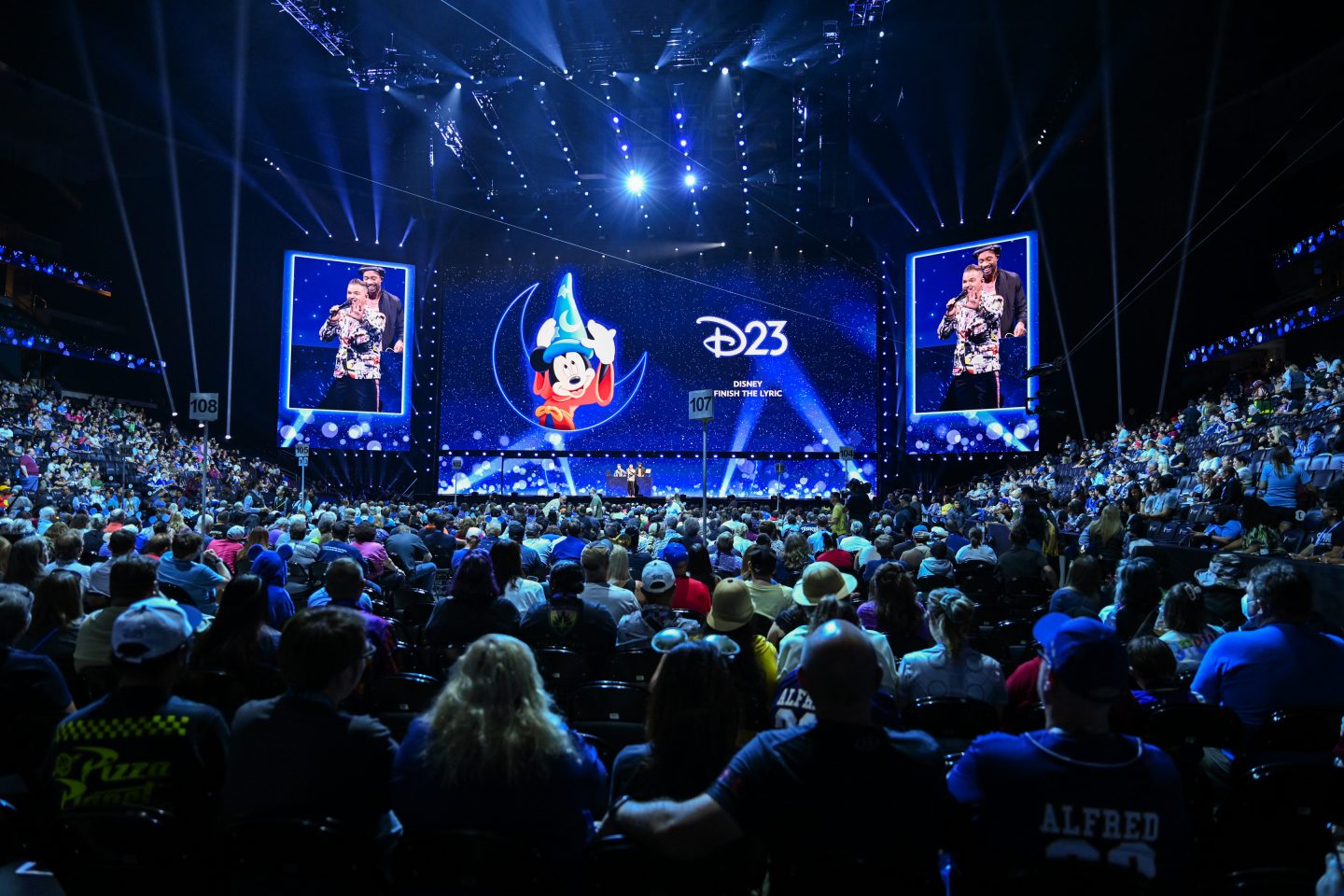 A brightly-lit stage in front of a large crowd of enthusiastic fans at D23: The Ultimate Disney Fan Event.